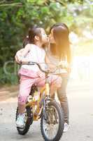 Child riding bike and giving kiss to mother, outdoor park.