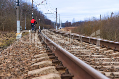 the man with the bike is on the sleepers of the railway, the cyclist is walking along the rail