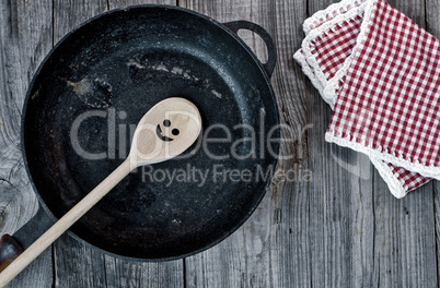 Black cast-iron frying pan with a wooden spoon on a gray wooden