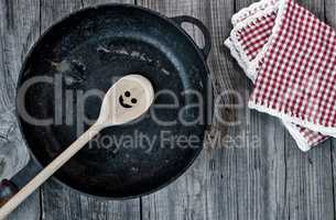 Black cast-iron frying pan with a wooden spoon on a gray wooden