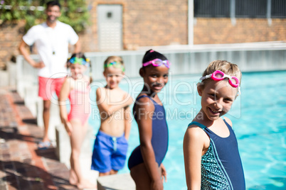 Little swimmers and male instructor standing at poolside