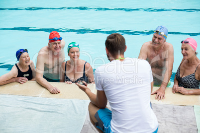 Male instructor assisting senior swimmers at poolside