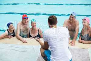 Male instructor assisting senior swimmers at poolside