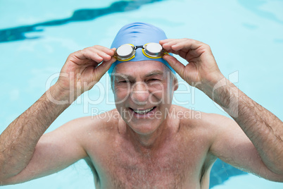 Senior man holding goggles in swimming pool