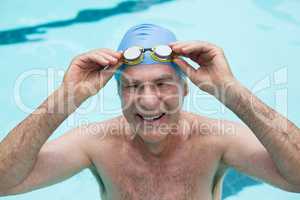 Senior man holding goggles in swimming pool