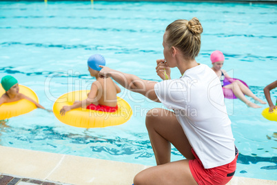 Lifeguard whistling while instructing children in swimming pool