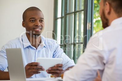 Businessman holding digital tablet while looking at colleague in restaurant
