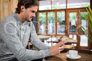 Handsome man using smartphone at table in coffee shop