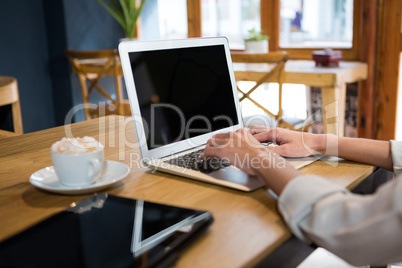 Cropped image of woman using laptop at table in careteria