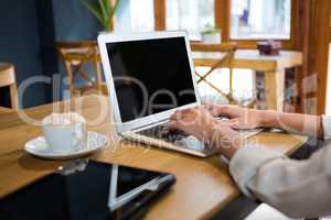 Cropped image of woman using laptop at table in careteria