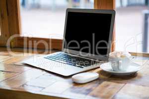 Laptop by coffee cup on table in cafe
