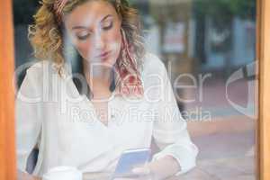Woman using smart phone in cafe seen through window