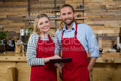 Smiling male and female baristas using digital tablet in coffee shop