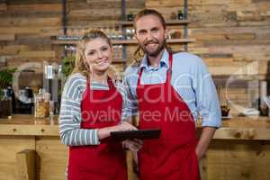 Smiling male and female baristas using digital tablet in coffee shop