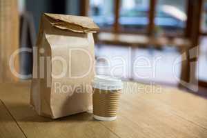 Disposable coffee cup and paper bag on table in cafe