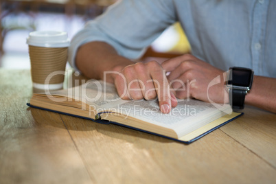 Man reading book at table in coffee shop