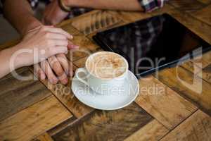 Couple holding hands with coffee cup and tablet PC on table in cafe