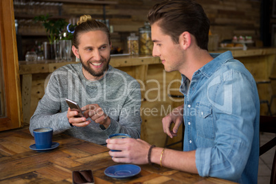 Happy man showing smart phone to friend in coffee shop