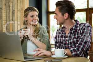 Man using laptop while looking at woman in coffee shop
