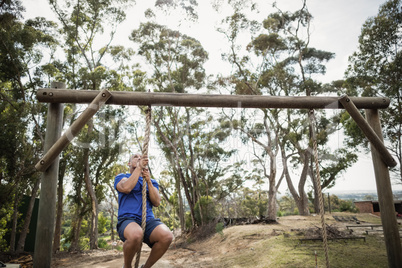 Fit man climbing down the rope during obstacle course