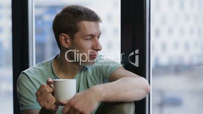 Relaxed young hipster drinking coffee near window