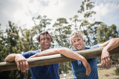 Smiling man and woman leaning on a hurdle during obstacle course
