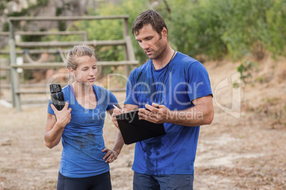 Trainer and woman discussing over clipboard during obstacle course