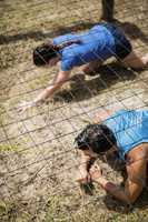 Fit man and woman crawling under the net during obstacle course