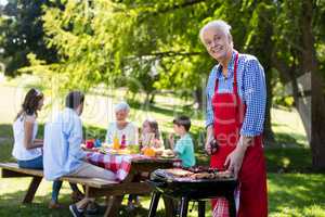 Senior man barbequing with family in background