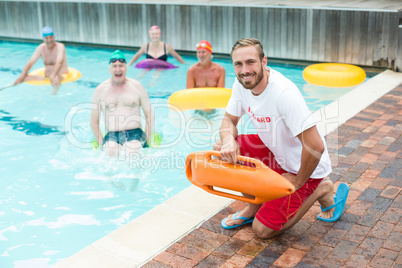 Male lifeguard crouching while swimmers swimming in pool