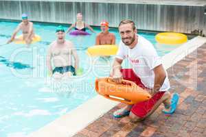 Male lifeguard crouching while swimmers swimming in pool