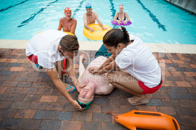 Rescue workers helping unconscious senior man at poolside