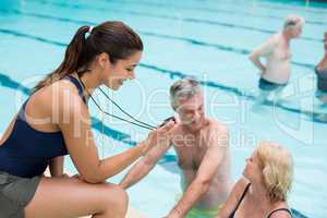 Young female trainer monitoring time of senior swimmers at poolside