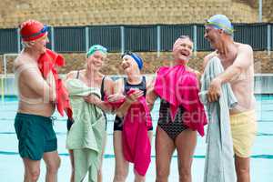 Happy senior swimmers wiping body with towels at poolside