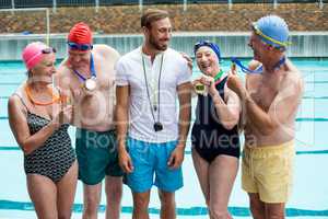 Swimmers showing medals to trainer at poolside
