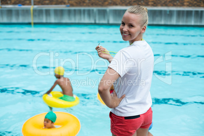 Confident female lifeguard holding whistle at poolside