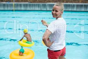 Confident female lifeguard holding whistle at poolside