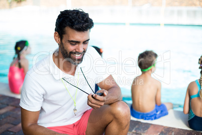 Male instructor watching stopwatch by children at poolside