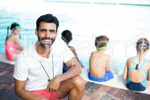 Male instructor crouching by children at poolside