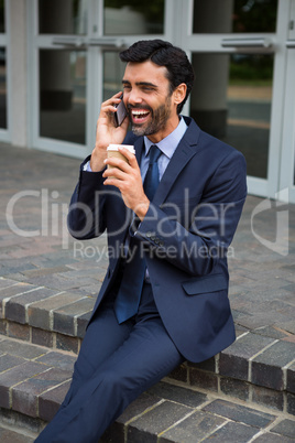 Businessman holding disposable coffee cup talking on mobile phone