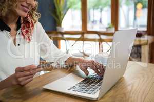Woman holding credit card while using laptop in coffee shop