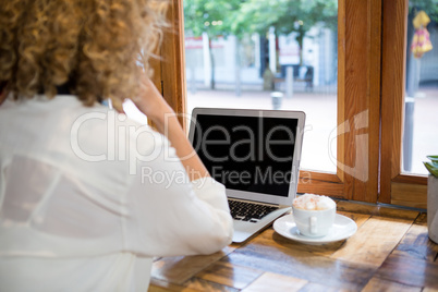 Rear view of woman using laptop in cafeteria