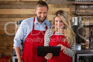 Smiling baristas using digital tablet in coffee shop
