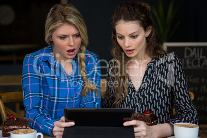 Shocked women using digital tablet in coffee shop