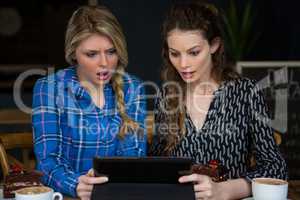 Shocked women using digital tablet in coffee shop