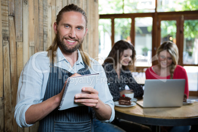 Portrait of happy male barista writing orders in coffee shop