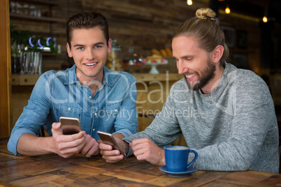 Smiling male hipsters using smart phones at table in coffee shop