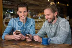 Smiling male hipsters using smart phones at table in coffee shop