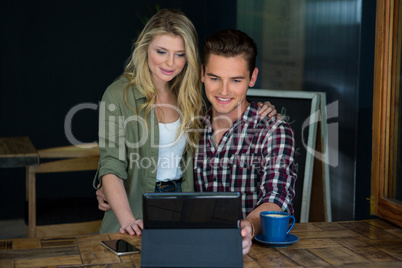 Smiling couple using tablet PC at table in coffee shop