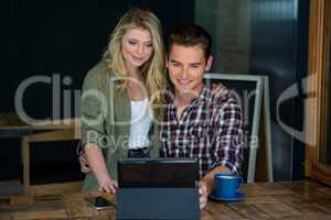 Smiling couple using tablet PC at table in coffee shop